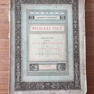 以下が含まれることがあります： 装飾的な縁取りと「NICOLAAS TULP. BIJDRAGE TOT DE GESCHIEDENIS DER GENEESKUNDE IN DE 17 Eeuw. E. H. M. THIJSSEN, ARTS, AMSTERDAM, J. C. SCHRODER」というタイトルが書かれた、ビンテージの書籍カバー