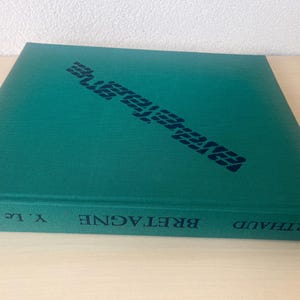 Op de afbeelding: Een turquoise boek met het woord "Bretagne" op de rug. De kaft toont "Bretagne" in een donkerblauwe, gestileerde letter. De auteur, Y. Le Gallo, en uitgever, Arthaud, zijn ook zichtbaar. Het boek is waarschijnlijk een reisgids of een geschiedenisboek.