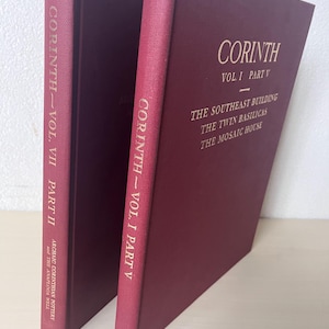 May include: Two maroon-colored books titled "Corinth." The book on the right is labeled "Vol. I Part V" and lists "The Southeast Building, The Twin Basilicas, The Mosaic House." The book on the left is labeled "Vol. VII Part II."