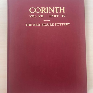 May include: A maroon book titled "Corinth Vol. VII Part IV The Red-Figure Pottery" in gold lettering. The book has a textured cover and is rectangular in shape. The book is lying on a light-colored surface.