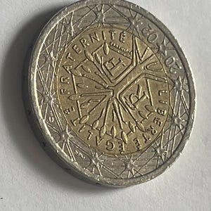 May include: A two-euro coin with a gold center and silver outer ring. The coin features the words "LIBERTE EGALITE FRATERNITE" and "2002" along with a design of a tree and other symbols.