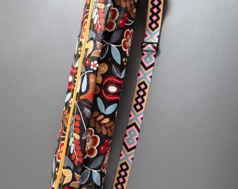 May include: A black yoga mat bag with a floral print and a pink and blue patterned strap. The bag has a yellow zipper.