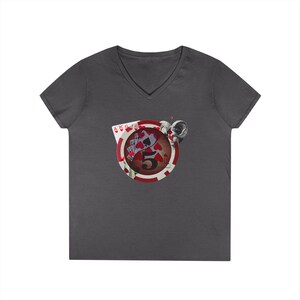 May include: Dark gray V-neck t-shirt featuring a poker chip design with playing cards and the number 5. The poker chip has a red and white border. A silver-colored object is on the right side of the poker chip.