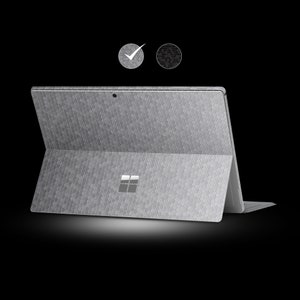 May include: A silver laptop with a textured, honeycomb-patterned surface. The laptop is open, displaying the screen and keyboard. The Microsoft logo is visible on the back. Two small circular icons are in the upper left corner.