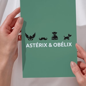 May include: A teal card with black silhouette icons of a winged helmet, moustache, helmet, and dog, with the text "ASTÉRIX & OBÉLIX" in white. The card is held by two hands.