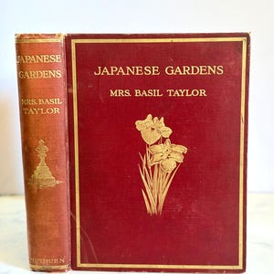May include: Two antique books titled "Japanese Gardens" by Mrs. Basil Taylor. The books have a red cover with gold lettering and a gold floral design. The spine of the book on the left is also red with gold lettering.