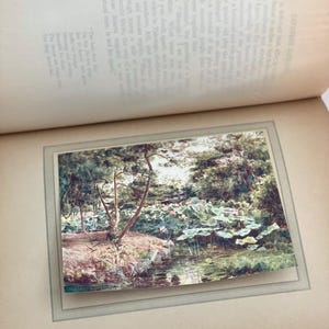 May include: A vintage print of a Japanese garden scene, featuring a pond with lily pads and pink lotus flowers. Trees line the water's edge, and the image is framed within a book page.