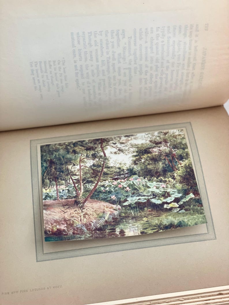 May include: A vintage print of a Japanese garden scene, featuring a pond with lily pads and pink lotus flowers. Trees line the water's edge, and the image is framed within a book page.