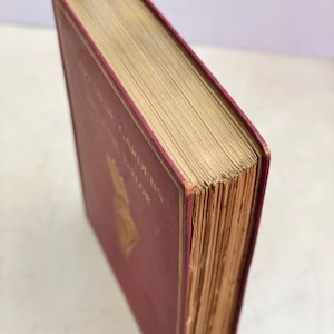 May include: A vintage book with a burgundy cover and gold lettering. The book's pages are aged, with a gold-colored edge. The title "English Gardens" is visible on the cover. The book is in good condition.