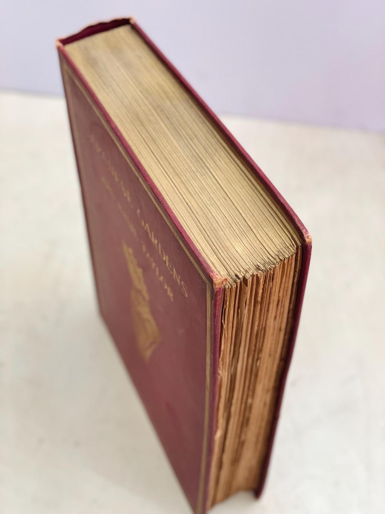 May include: A vintage book with a burgundy cover and gold lettering. The book's pages are aged, with a gold-colored edge. The title "English Gardens" is visible on the cover. The book is in good condition.