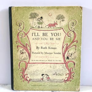 May include: A green book cover with a pink and white illustration of children playing. The title of the book is "I'll Be You And You Be Me" by Ruth Krauss, with illustrations by Maurice Sendak.