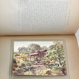May include: A vintage print of a Japanese garden scene, featuring a traditional wooden structure over a pond. The artwork showcases lush greenery, trees, and a serene landscape, with text from a book visible.