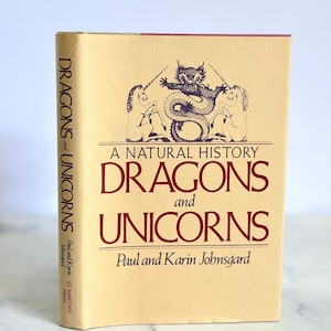 May include: A hardcover book titled "Dragons and Unicorns" with a cream-colored cover. The cover features a dragon and unicorn illustration in dark brown, with the title in a matching font. The book's spine also displays the title.