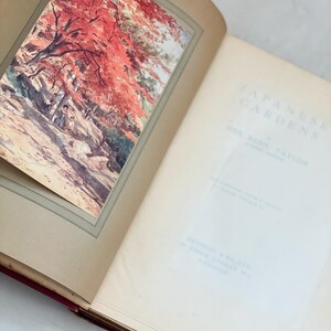 May include: Open book with a color illustration of a Japanese garden scene with red trees. The book's title page reads "Japanese Gardens" by Mrs. Basil Taylor. The book is open to a blank page.