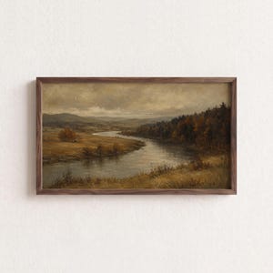May include: A landscape painting in a dark wood frame depicting a winding river flowing through a golden meadow and dense forest under a cloudy sky. The artwork features muted earth tones, including shades of brown, tan, and deep green.