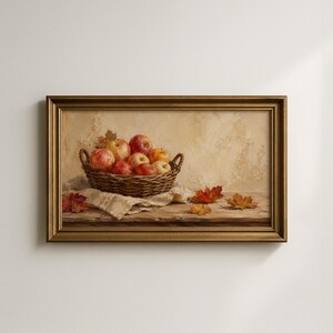 May include: A framed oil painting depicting a woven wicker basket filled with red and yellow apples resting on a textured cloth. Several fallen autumn leaves in shades of orange, red, and gold are scattered on the wooden surface nearby.