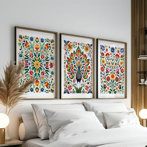 May include: Three framed prints with colorful folk art designs. The center print features a peacock with a vibrant tail. The prints are hung on a white wall above a bed with white bedding and a green throw.