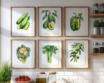 Puede incluir: Conjunto de seis impresiones de acuarela enmarcadas que presentan varias verduras y frutas verdes, incluyendo pepinos, aguacates, pimientos, coliflor, apio y aceitunas. Las impresiones se muestran en una pared de azulejos blancos sobre una encimera de madera.