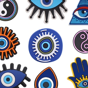 Pu&ograve; includere: Assortimento di ciondoli portafortuna con occhio turco colorati con diversi design, tra cui un simbolo yin yang, una mano con un occhio e una forma a goccia.
