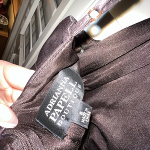 May include: A close-up of a dark brown dress with a thin strap. The tag reads "Adrianna Papell Boutique" and "Made in China". The dress is size 6.