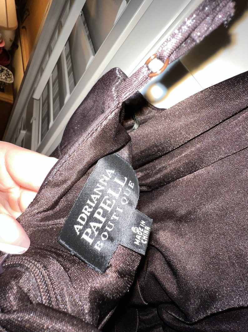 May include: A close-up of a dark brown dress with a thin strap. The tag reads "Adrianna Papell Boutique" and "Made in China". The dress is size 6.
