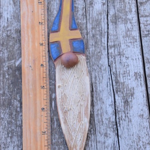 May include: A ceramic gnome ornament with a yellow and blue design, resembling the Swedish flag. The gnome is approximately 8 inches tall and has a white beard.