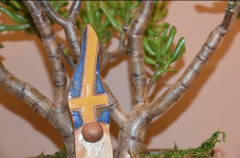 May include: A ceramic gnome figurine with a yellow, blue and white hat. The hat is painted with the colours of the Swedish flag.