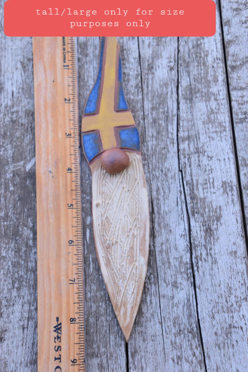 May include: A ceramic gnome figurine with a white beard and a blue and yellow hat. The hat is painted with the colors of the Swedish flag. The gnome is approximately 8 inches tall.