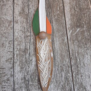 May include: A brown leather knife with a white, green, and orange design. The knife has a silver-colored design of a wheat stalk on the blade.