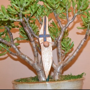 May include: A ceramic gnome figurine with a white beard and blue and white patterned hat. The gnome is standing in a pot with a green plant.