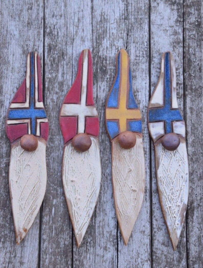May include: Four ceramic gnomes with painted flags on their hats. The flags are the colors of Norway, Denmark, Sweden, and Finland. The gnomes are white with a textured beard and brown noses.