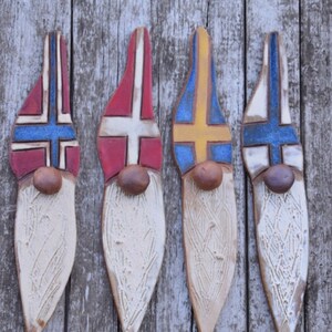 May include: Four wooden gnome ornaments painted with the flags of Norway, Denmark, Sweden, and Finland. Each gnome has a white beard and a brown hat.