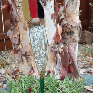 May include: A ceramic gnome garden stake with a red, gold, and black hat and a white beard. The gnome is standing in a pot of green succulents.