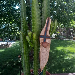 May include: A ceramic garden gnome figurine with a blue and white patterned hat and a white beard. The gnome is standing in a pot with a green cactus plant.