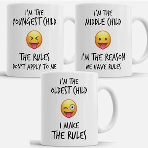 Peut inclure: Trois tasses en céramique blanche avec du texte noir et un emoji jaune. Les tasses indiquent "Je suis le plus jeune enfant les règles ne s'appliquent pas à moi", "Je suis l'enfant du milieu Je suis la raison pour laquelle nous avons des règles", et "Je suis l'aîné Je fais les règles".
