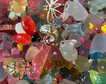 Op de afbeelding: Een verzameling kleurrijke, doorschijnende plastic bedels in verschillende vormen, waaronder dieren, insecten en bloemen. De bedels zijn perfect om een ​​toets van whimsy toe te voegen aan sieraden, sleutelhangers of andere knutselprojecten.