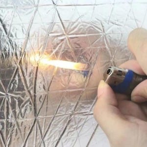 May include: A silver, diamond-patterned heat shield material being tested with a lighter. The flame from the lighter is touching the material, demonstrating its heat resistance.