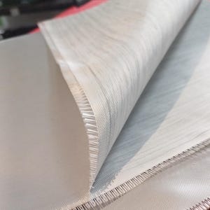 May include: Close-up of a white fabric with a woven texture. The fabric is folded over, revealing a slightly darker shade of white on the underside.