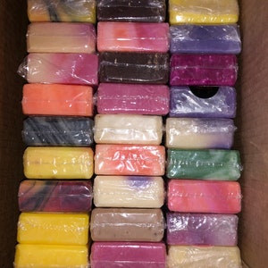 Peut inclure: Une bo&icirc;te en carton remplie de savons emball&eacute;s individuellement. Les savons sont de diff&eacute;rentes couleurs, notamment jaune, rose, violet et marron. Chaque savon est rectangulaire et envelopp&eacute; dans du plastique transparent.