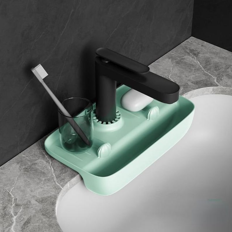 May include: A mint green sink organizer with a black faucet, a toothbrush, a clear glass, and a bar of soap. The organizer has a rectangular shape with rounded edges and two small holders.