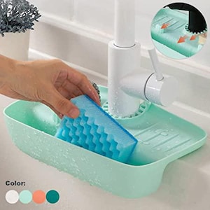 May include: A light green sink caddy with a blue sponge. The caddy is designed to hold a sponge and sits near a white faucet. The sponge has a textured surface. The caddy has a drainage design.