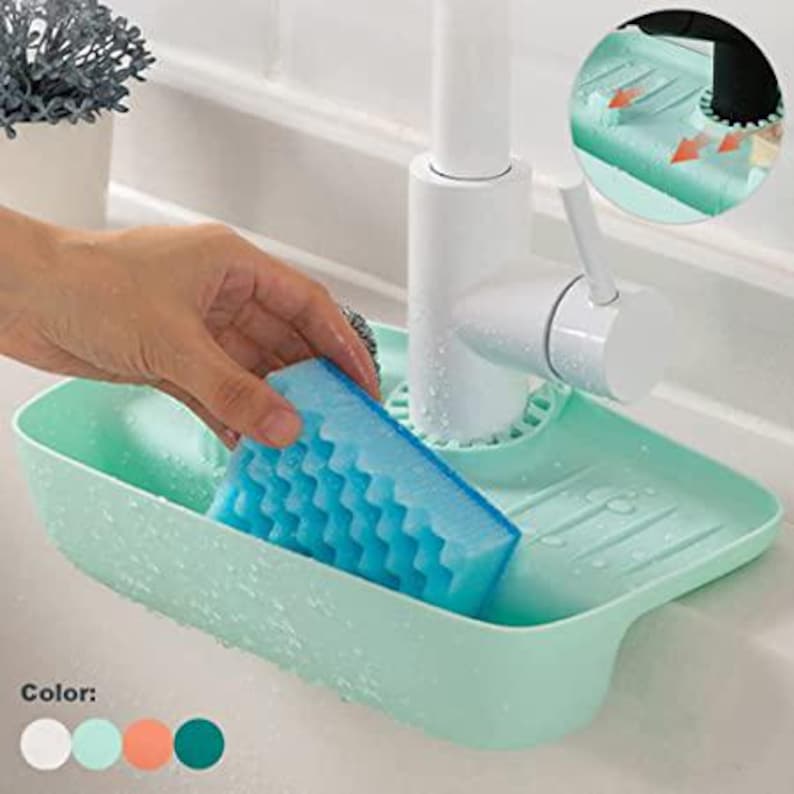 May include: A light green sink caddy with a blue sponge. The caddy is designed to hold a sponge and sits near a white faucet. The sponge has a textured surface. The caddy has a drainage design.