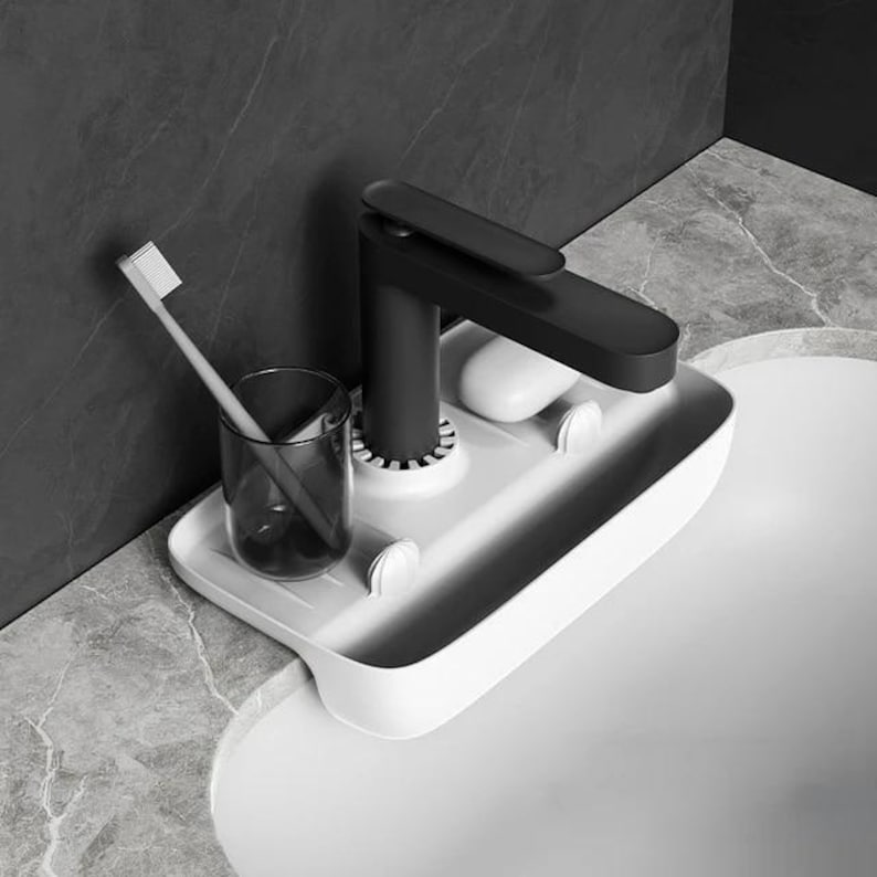May include: A white plastic sink organizer with a black faucet, a toothbrush, and a glass. The organizer has a soap dish and a slot for a toothbrush. The faucet is black and has a modern design.