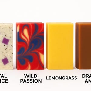 Peut inclure: Quatre savons artisanaux rectangulaires. Les barres sont &eacute;tiquet&eacute;es "Petal Dance", "Wild Passion", "Lemongrass" et "Dragon Amber". La barre "Petal Dance" est blanc cass&eacute; avec des carr&eacute;s violets. "Wild Passion" a des tourbillons rouges, bleus et blancs. "Lemongrass" est jaune et "Dragon Amber" est marron.