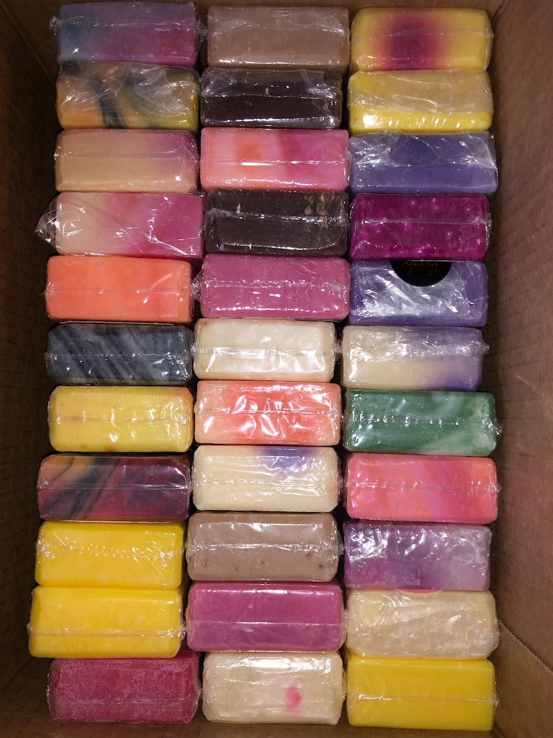 Peut inclure: Une bo&icirc;te en carton remplie de savons emball&eacute;s individuellement. Les savons sont de diff&eacute;rentes couleurs, notamment jaune, rose, violet et marron. Chaque savon est rectangulaire et envelopp&eacute; dans du plastique transparent.