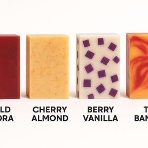 Peut inclure: Quatre savons artisanaux rectangulaires. Les barres sont &eacute;tiquet&eacute;es "Wild Flora", "Cherry Almond", "Berry Vanilla" et "Tiki Banana". Les couleurs des savons comprennent le rouge, le jaune, le blanc avec des carr&eacute;s violets et l'orange avec des tourbillons rouges.