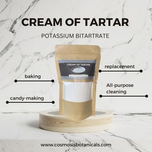 Könnte beinhalten: Ein Kraftpapierbeutel mit Weinstein, Kaliumbitartrat, auf einem Holzständer. Das Etikett lautet "Cream of Tartar" und listet Verwendungen auf: Backen, Süßwarenherstellung, Ersatz und Allzweckreinigung. Die Website www.cosmosisbotanicals.com ist sichtbar.
