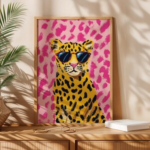 May include: A framed print of a yellow and black leopard wearing sunglasses against a pink and white background.