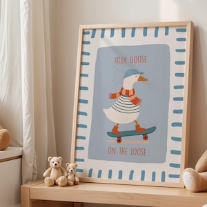 May include: A framed art print depicting a cartoon goose skateboarding. The goose is wearing a blue cap, striped shirt, and scarf. The print has a light blue background with the words "SILLY GOOSE ON THE LOOSE". The frame is light wood.