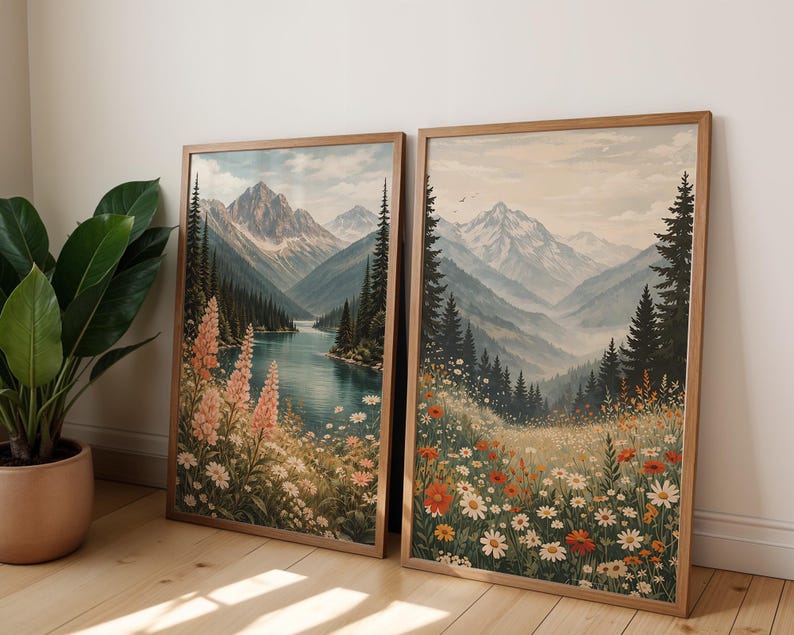 May include: Two framed landscape art prints. One features a river scene with mountains and pink flowers. The other depicts a meadow with wildflowers and mountains. Both are in wooden frames, creating a cohesive set.